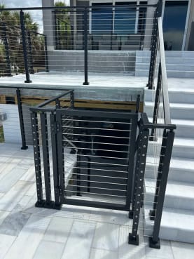 A black cable railing gate and posts sit at the base of white marble exterior steps.