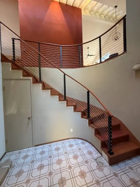 Black posts and a curved wood handrail with stainless cables follow a sweeping curved stair to a curved balcony.