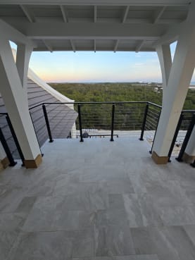 White timber braces frame a tiled covered balcony with black cable railing looking out over forest.