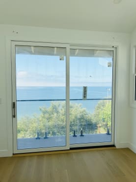 A sliding door frames a balcony with spigot-mounted glass railing and black top cap overlooking the ocean.