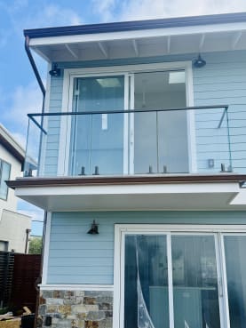 Front view of a small balcony with spigot-mounted frameless glass and black top cap on a pale blue clapboard house.