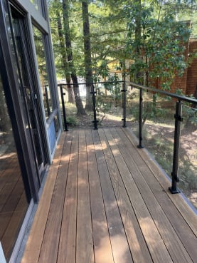 A narrow wood deck runs beside large windows with a black post-to-post glass railing set among redwoods.