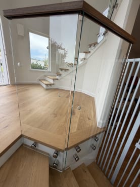 Stainless standoff pins hold frameless glass with a wood cap around an angled oak landing above the stair.