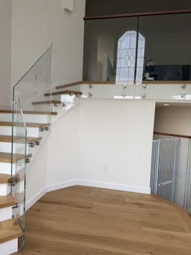 Frameless glass on stainless standoff pins follows an oak stair and continues along the loft fascia beneath an arched window.