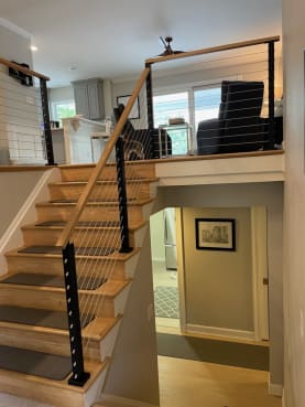 Black-post cable railing with a wood handrail climbs a split-level stair into a bright living area.
