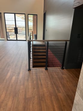 Black-post cable railing with wood cap guards a stair opening off a wood-floored entry.