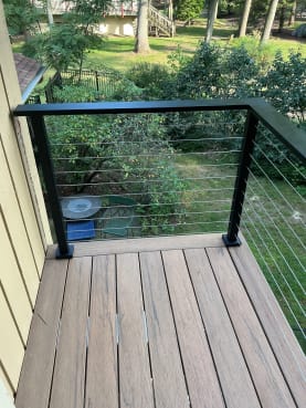Black-post cable railing frames a small composite deck corner overlooking a garden.