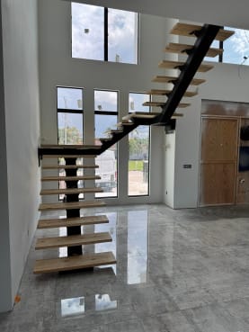 Black mono-stringer floating stair with light wood treads turns at a landing in a double-height room with tall windows.