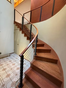 Black posts and stainless horizontal infill follow a curved Brazilian cherry staircase with a wood handrail.