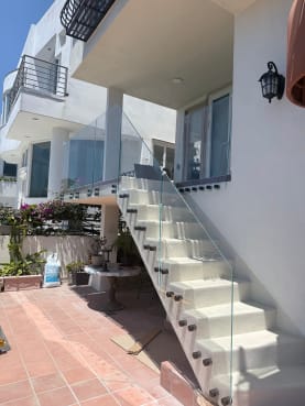 Clear glass on bronze standoff pins guards a white exterior stair beside a tiled patio.