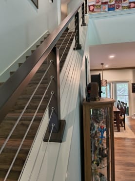 Burnished bronze cable posts and rail run along an angled knee wall above a wood stair.