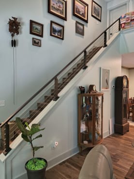 Bronze cable railing tops a white knee wall along a long stair beneath framed art.