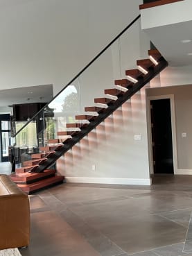 Black mono stringer floating stair with reddish wood treads, frameless glass guard and plinth steps over large-format tile.