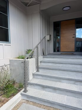 Gray stone front entry steps with a gray aluminum cable railing leading to a wood front door.
