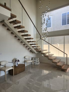 Oak floating stair with white stringer and frameless glass with wood handrail rising beside a crystal chandelier over polished marble.