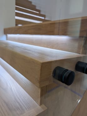 Close detail of black standoff pins holding glass to thick oak treads with under-tread LED lighting.