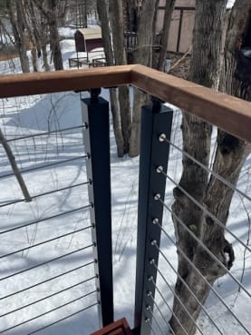 Black slim side mount cable posts with an Ipe handrail on a deck overlooking snowy woods.
