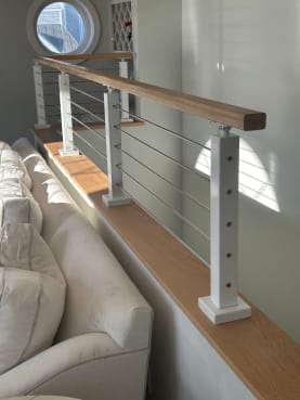 White posts with cable infill and a wood cap rail sit atop a half wall beside a living room sofa.