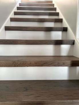 Dark oak thick-nose replacement treads over white risers climb a narrow stair.