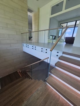 Thick oak treads with LED under-lighting and a frameless glass railing topped by a wood handrail in a bright modern home.