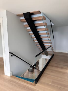 Light oak treads on a black mono stringer with frameless glass running from floor toward the ceiling.