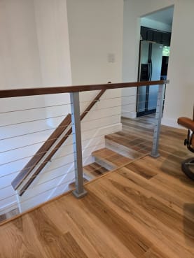 Silver posts and stainless cables with a wood top rail line a short interior stair and landing over oak floors.
