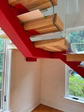 Underside view of a bright red mono stringer carrying thick wood floating treads with a glass railing edge.