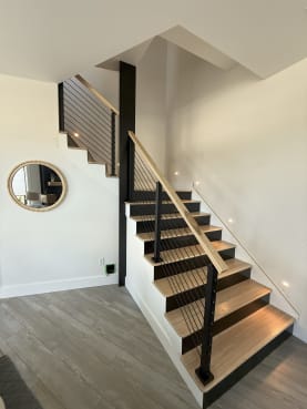 Black posts with horizontal rods and a light oak handrail follow a switchback stair with oak treads and black risers.