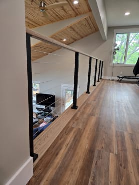 Black-post cable railing with a wood handrail runs along a wood-floored loft overlooking the room below.