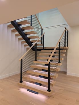 Front view of a white oak FLIGHT Mono switchback with under-tread LED glow and black cable railings on both sides.