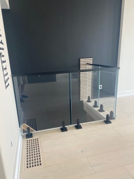 Frameless glass on black talons with a black cap guards a stair opening against a dark accent wall.
