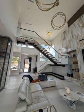 Black FLIGHT Mono floating stair with frameless glass rising through a double-height room with marble walls