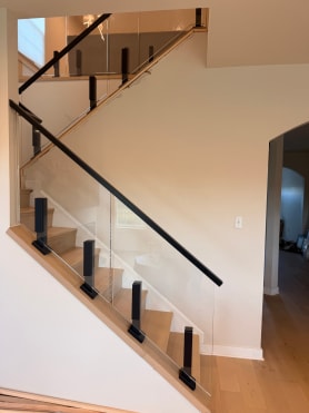 Black talon clamps hold glass panels along a stair stringer with a black handrail.