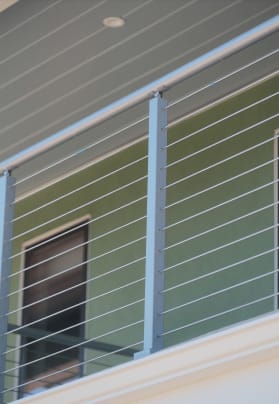 Silver cable railing with round top rail on a balcony beside a green-sided home.