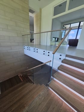 Frameless glass on standoff pins with a wood top cap along a framed stair with LED-lit treads