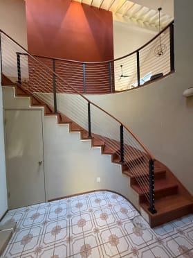 Curved stair and balcony with black posts and cable infill in a two-story foyer.