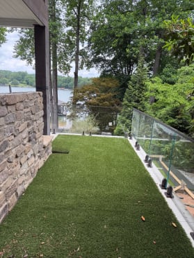 Frameless glass on burnished bronze surface talons edges a turf terrace overlooking a lake.