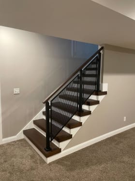 Stained thick-nose treads with white risers pair with a black perforated panel railing and wood cap in a basement.
