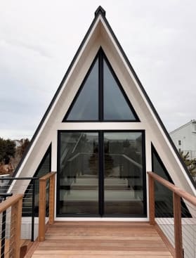 Cable railing with wood posts and cap frames an Ipe deck leading to a modern A-frame glass facade.