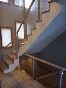 Silver posts with cable infill and wood handrails follow a switchback stair above a tiled entry.