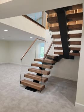 Thick wood treads on a black mono stringer rising through winders beside frameless glass with a wood handrail.