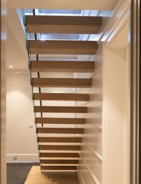 Straight run of white oak cantilever treads with frameless glass in a paneled stairwell
