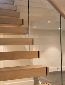 Close view of white oak cantilever treads behind a frameless glass railing