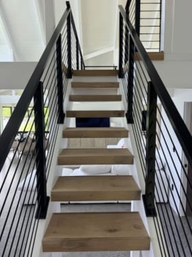 View up an open-riser oak stair flanked on both sides by black horizontal rod railing.