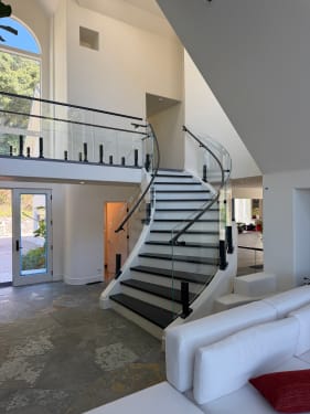 Grand curved white staircase with dark treads and a black-post glass railing continuing along the open loft.