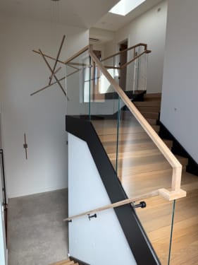 Switchback white oak stair with frameless glass guard, black fascia and an oak handrail in a white stairwell.