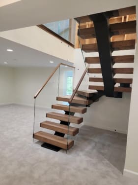 Thick wood treads on a black mono stringer rising through winders beside frameless glass with a wood handrail.