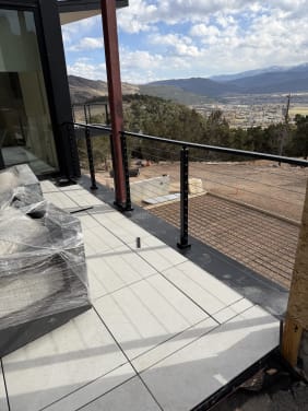 Black cable railing on a tiled deck overlooking a valley town and distant mountains