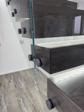 Detail of frameless glass on round standoff pins attached to dark cantilever treads with LED lighting