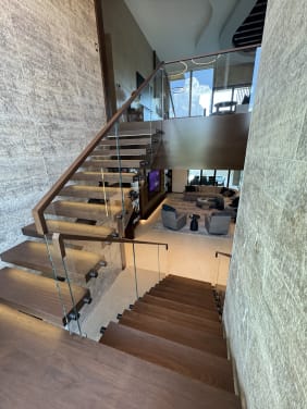 Walnut floating stair with standoff-pin glass and a wood handrail overlooking a modern living room